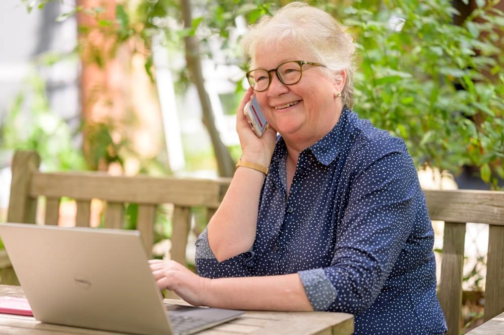 Iets oudere dame telefonerend achter de laptop