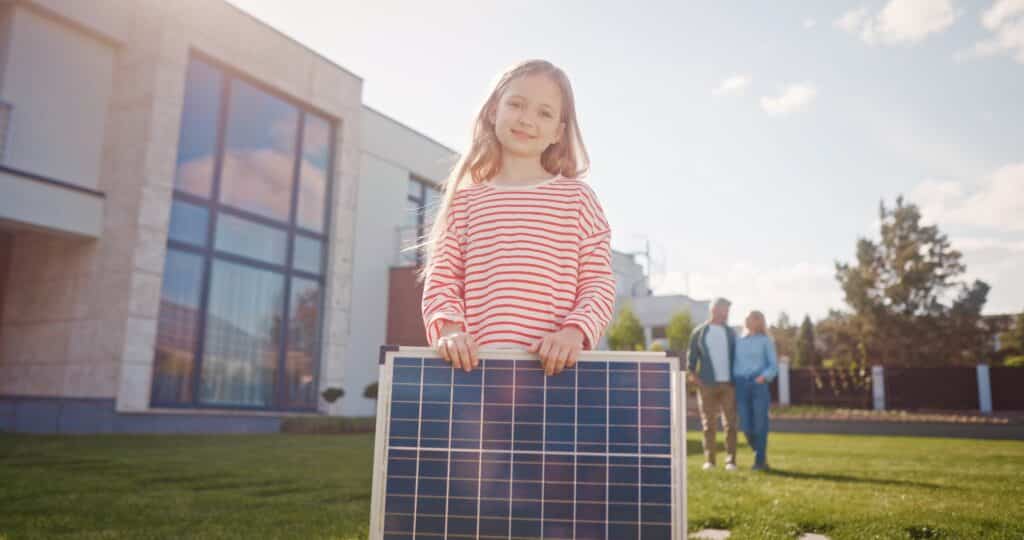 Blij meisje met zonnepaneel kijkt in de camera met blije ouders op de achtergrond